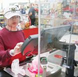 Cashier Baby San wears a face shield and gloves and stands behind a plexiglass shield as she scans items at grocery store Super Cao Nguyen, Friday, March 27, 2020, in Oklahoma City, due to concerns over the COVID-19 virus. The new coronavirus causes mild or moderate symptoms for most people, but for some, especially older adults and people with existing health problems, it can cause more severe illness or death. (AP Photo/Sue Ogrocki)